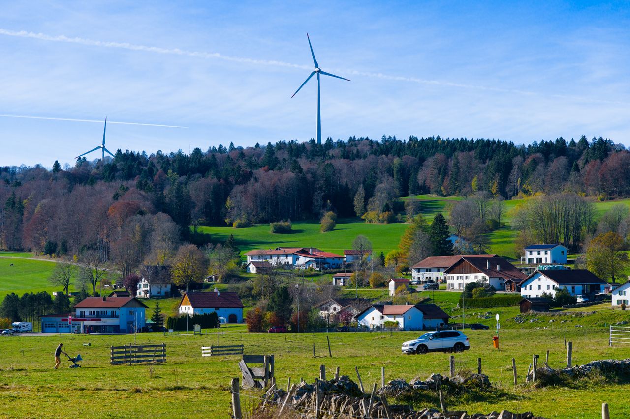 Picturesque Les Breuleux village with modern wind turbines and lush green fields under a clear blue sky.