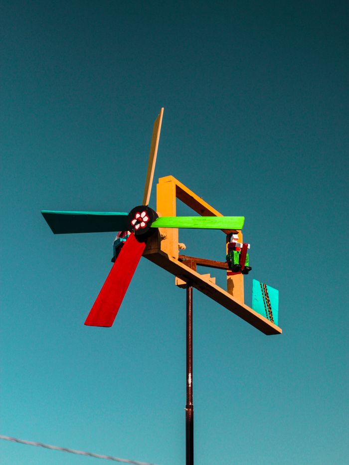 gallery-05 Vibrant handmade windmill with colorful blades set against a clear blue sky, symbolizing eco-friendly energy.